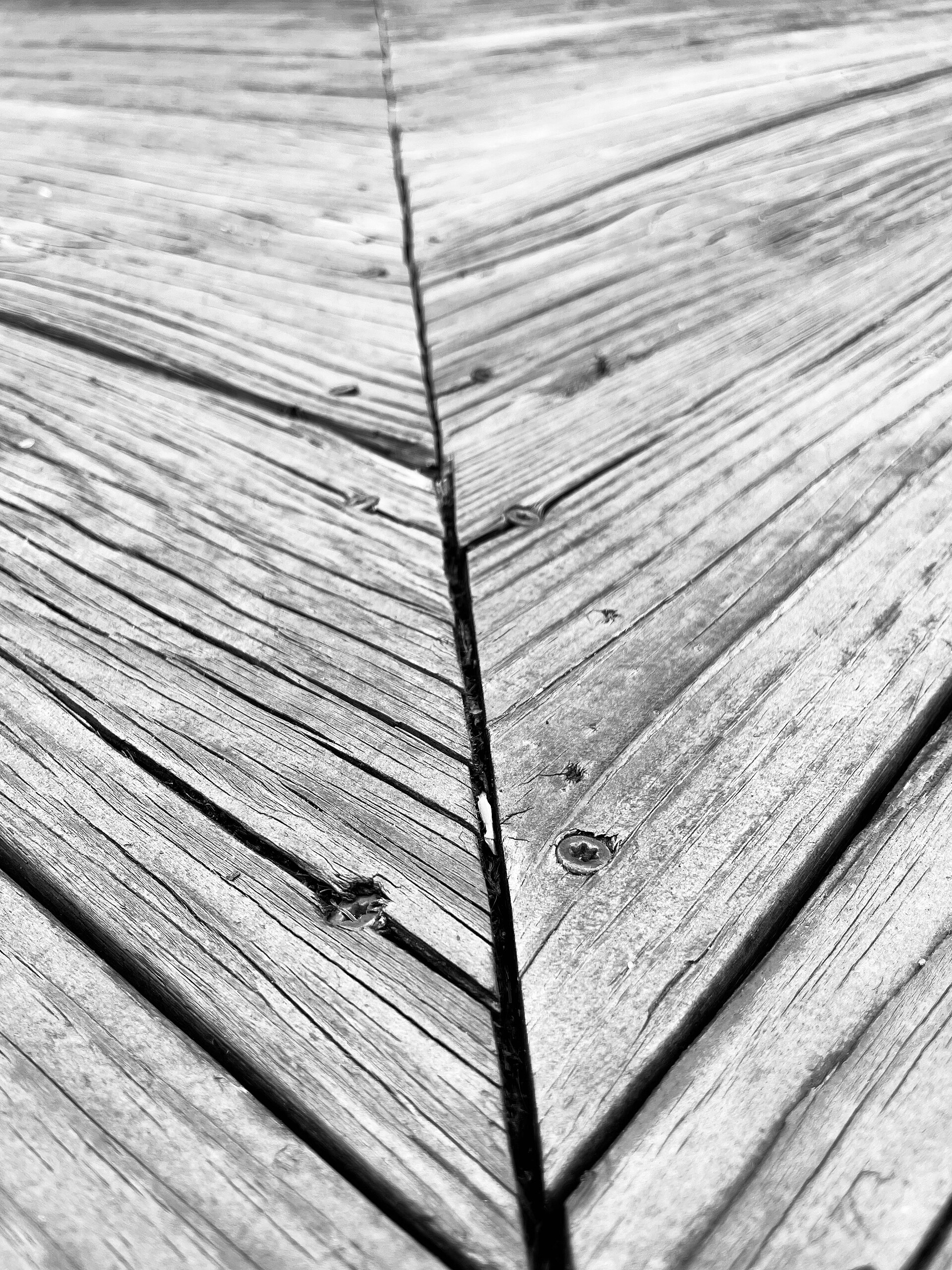 Close-up of weathered wooden deck boards meeting at a joint, with recessed deck screws.