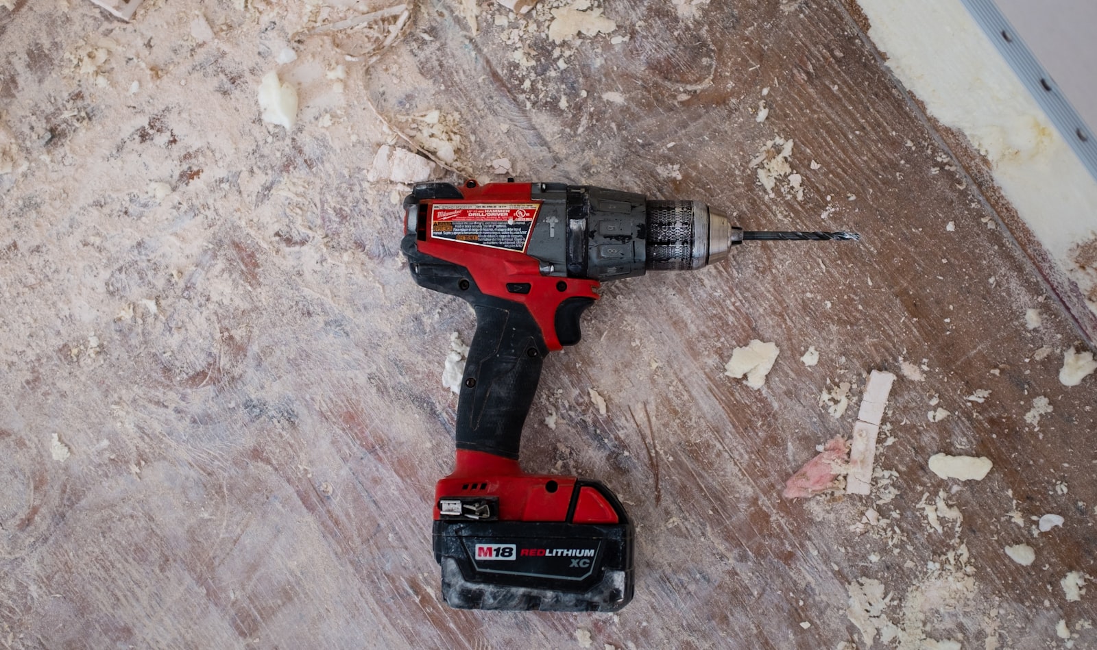 A used Milwaukee M18 drill on a dusty job-site floor.